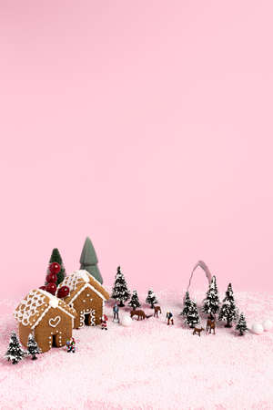 Creative Christmas scene made with with ginger houses, Santa Claus, trees, snow and reindeers on pink pastel color background. Minimal New Year concept.の写真素材