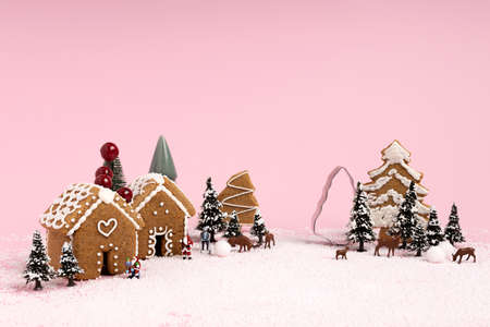 Creative Christmas scene made with with ginger houses, Santa Claus, trees, snow and reindeers on pink pastel color background. Minimal New Year concept.の写真素材