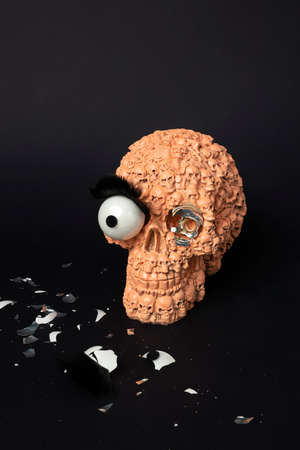 Orange skull with broken glass eye on black. Minimal gothic concept. Halloween creative background.