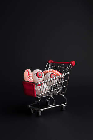 Creative layout made with eyeballs in shopping cart on black background. Minimal Halloween shopping background. Invitation card, party, copy space. Flat lay.の写真素材