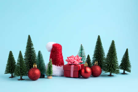 Christmas scene made with miniature pine trees, gifts, ornaments and Santa's hat on blue background....