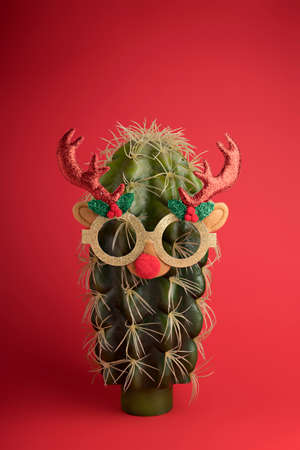 Creative Christmas layout made with cactus wearing sunglasses and antlers on a red background. Minimal New Year season concept. Celebration, greeting card, banner.の写真素材