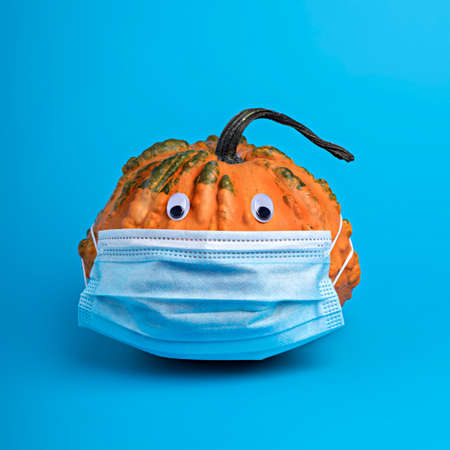 Creative fall layout made of pumpkins with surgical mask on a blue background. Autumn, Halloween or Thanksgiving isolation, coronavirus and quarantine concept. Flat lay, top view.の写真素材