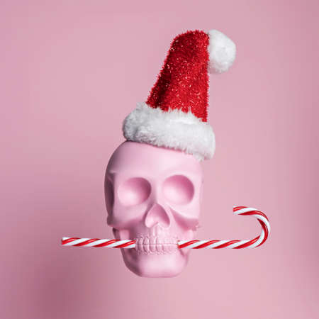 Christmas layout with pink skull wearing Santa's cap and biting candy cane on bright pink background. Minimal New Year's seasonal concept. Holiday greeting card.の写真素材