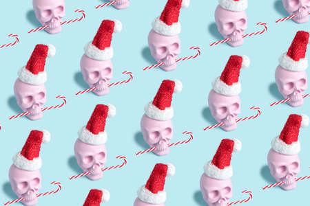 Christmas pattern layout with pink skull wearing Santa's cap and biting candy cane on bright blue background. Minimal New Year's seasonal concept. Holiday greeting card, flat lay, top view.の写真素材