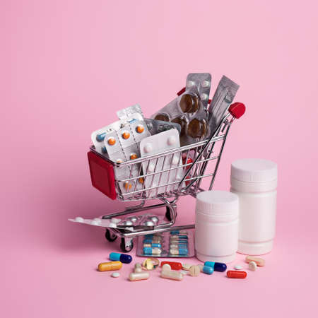 Creative medical layout made with pharmaceutical medicine pills, tablets, capsules in shopping trolley on pink background. Minimal modern pharmacy or health care concept. Flat lay.の写真素材
