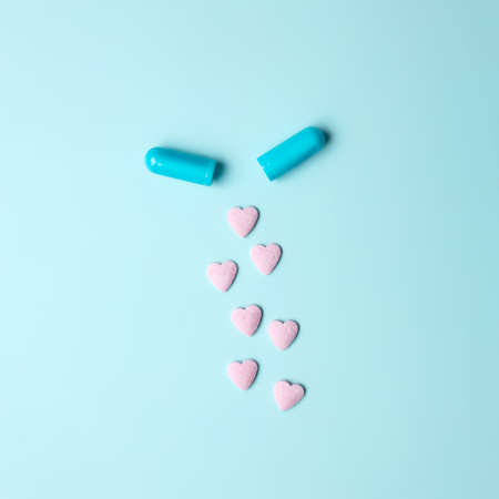 Opened medicine drug capsule with hearts spilling over on a blue background. Minimal medicine healthcare or pharmacy concept. Copy space, flat lay.の写真素材
