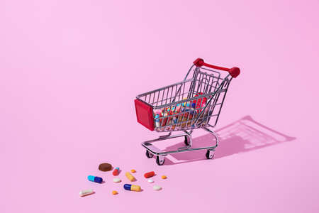 Creative medical layout made with pharmaceutical medicine pills, tablets, capsules in shopping trolley on pastel pink background. Minimal modern pharmacy or health care concept with trend shadows.の写真素材