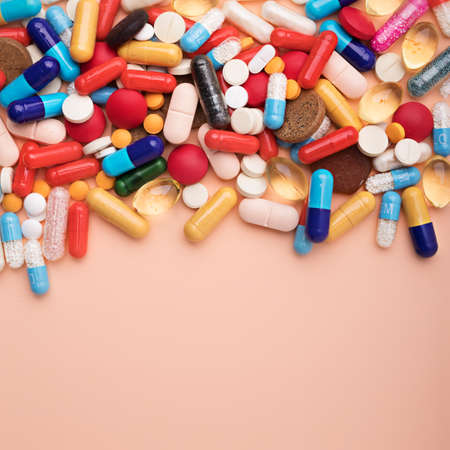 Creative layout made with heap of pills and capsules on pastel orange background. Pharmaceutical,...