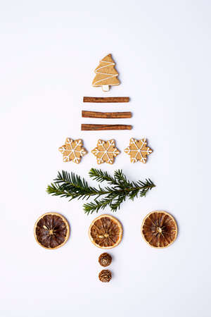 Christmas tree made with fir, cinnamon sticks, dried lemon and cookies on bright background. Minimal holiday and celebration creative concept. New year or Christmas postcard or invitation. Flay lay.の写真素材