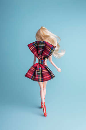 Doll wearing high heels and bow tie dress on blue background. Minimal fashion or beauty concept.の写真素材