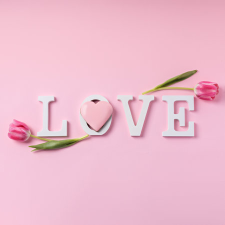 Word Love decorated with tulips on pink background. Modern Valentine's Day concept. Creative greeting card layout. Flat lay, top view.の写真素材