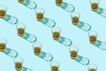 Pattern made of drink, glasses and beverage with trend shadows on blue background. Beautiful reflections from glass on backdrop. Minimal summer refreshment or alcohol layout. Flat lay.の写真素材