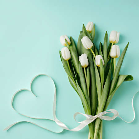 Spring floral bouquet arrangement made with fresh white tulips and heart shaped ribbon on pastel...