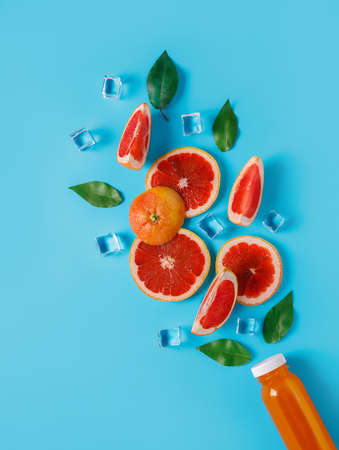 Colorful smoothie juice in glass bottle surrounded with orange slices, fresh leaves and ice on blue background. Creative fruit, healthy eating or summer vegetarian concept. Flat lay.の写真素材