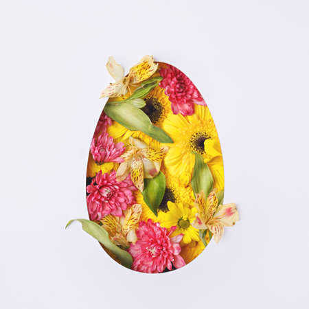 Easter egg made with spring fresh flowers on white background. Spring and Easter art holiday concept with copy space. Flat lay.の写真素材