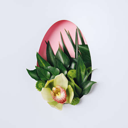 Easter egg shape made of green leaves and orchid flower on bright background. Minimal spring bloom concept. Holiday visual trend. Flat lay.の写真素材
