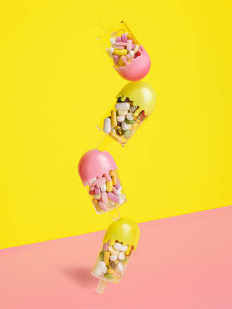 Vertically assorted ice cream filled with various pills and tablets on two tone pink and yellow background. Creative health care or summer sweet food concept. Minimal flat lay.の写真素材