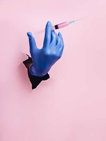 Hand with syringe breaking in through a black hole on yellow background. Minimal Coronavirus,...