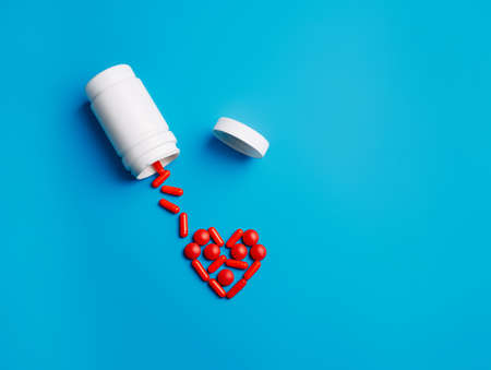Bottle and spilled red pills forming heart shape on vibrant blue background. Minimal health care, supplement, vitamins or pharmacy concept. flu visual trend. Flat lay, top view.の写真素材