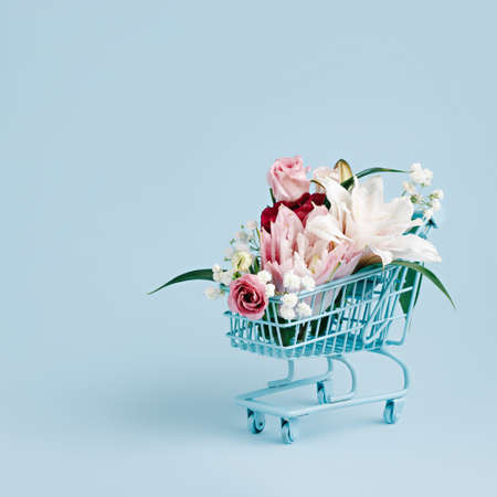 Shopping trolley with flowers on pastel blue background. Flower delivery concept with copy space. Sale, shopping for the holidays, Mothers Day, Women's Day, Valentines Day or Birthday.の写真素材