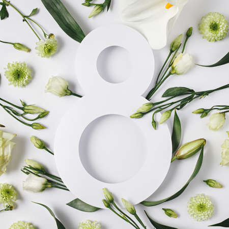 Number 8 surrounded with fresh gerbera, calla and rose flowers with green leaves on bright white...