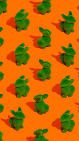 Pattern with green bunnies against vibrant orange background. Minimal Easter holiday concept. Abstract visual concept with rabbits. Flat lay, top view.の写真素材