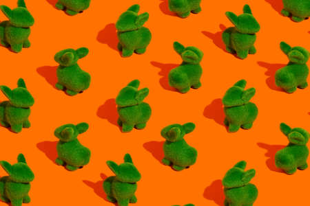 Pattern with green bunnies against vibrant orange background. Minimal Easter holiday concept....