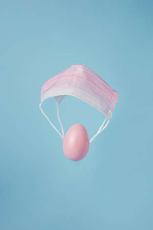 Pink Easter eggs flying on medical masks as if by parachute against pastel blue background.の写真素材