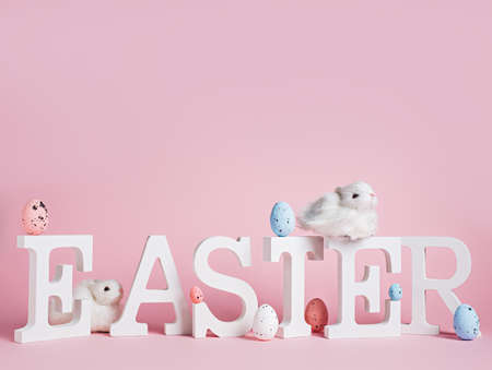 Word Easter made with alphabet, painted eggs and fluffy bunny rabbit against pastel pink background. Minimal Easter holiday celebration. Creative greeting card with copy space.の写真素材