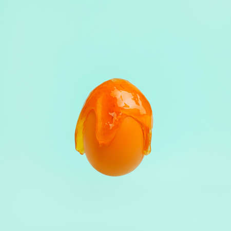 Orange egg with dripping slime paint against vibrant green background. Creative Easter holiday or food concept. Abstract spring holiday idea.の写真素材