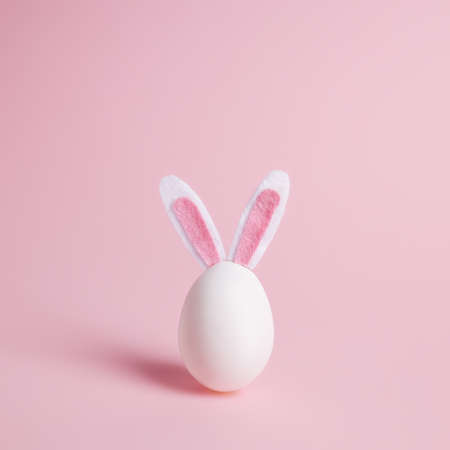Easter egg with bunny ears on pastel pink background. Minimal Easter celebration concept or greeting...