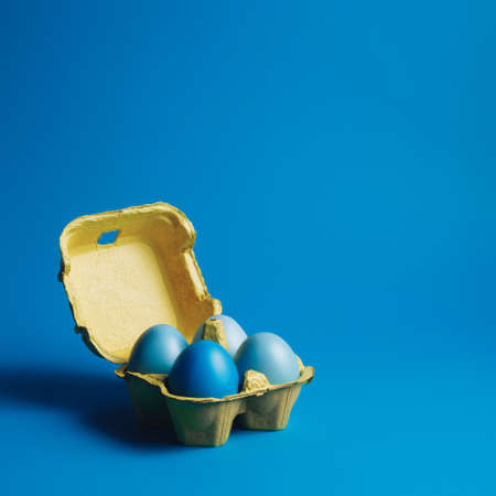 Yellow carton egg box with blue gradient painted eggs against vibrant blue background. Minimal Easter concept. Creative organic food composition.の写真素材