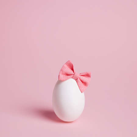 Cute Easter egg with bow tie headband on pastel pink background. Minimal Easter or food concept.の写真素材