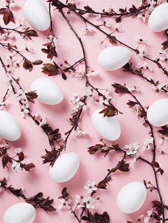 Spring texture with white eggs and cherry blossom branches on pastel pink background. Minimal trendy...