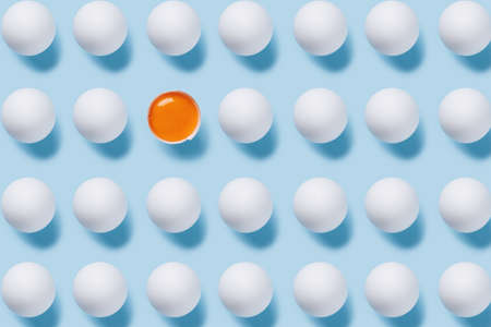 White eggs pattern with one broken egg on a pastel blue background. Minimal Easter, food or individuality concept. Flat lay, top view.の写真素材