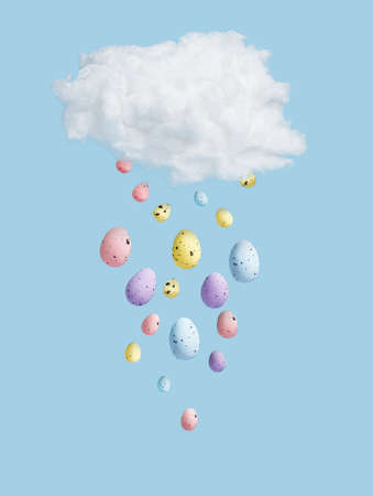 White cotton cloud with Easter eggs rain on bright blue background. Creative concept. Flat lay, top...