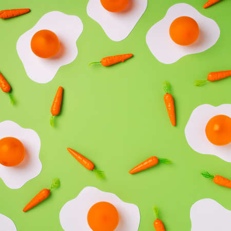 Pop art border frame with fried eggs and carrots against vibrant green background. Minimal food or Easter concept with copy space for text. Flat lay, top view.の写真素材