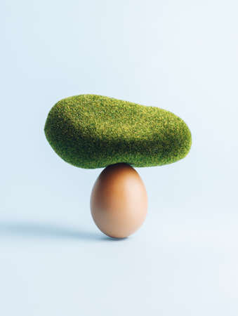 Natural egg with mossy stone on top of it against pastel blue background. Minimal balance and strength concept. Creative Easter or food layout.の写真素材