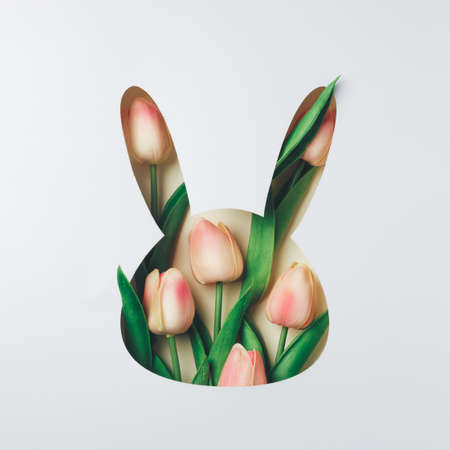 Creative Easter layout with fresh tulip flowers and leaves on bright white and beige paper background. Spring natural concept. Bunny shape Easter holiday minimal composition. Flat lay, top view.の写真素材
