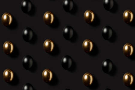 Black and gold eggs pattern over dark black background. Minimal luxury Easter concept. Trendy layout representing investments, savings and pensions. Flat lay, top view.の写真素材