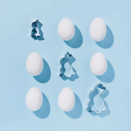 Creative geometrical layout made of white eggs and rabbit shaped mold on pastel blue background....