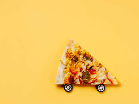 Pizza slice moves with wheels against pastel orange background. Creative food delivery concept. Restaurant or pizzeria banner. Flat lay, top view.の写真素材