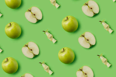Pattern made with fresh green eaten apples and halves on the green background. Minimal organic fruit...