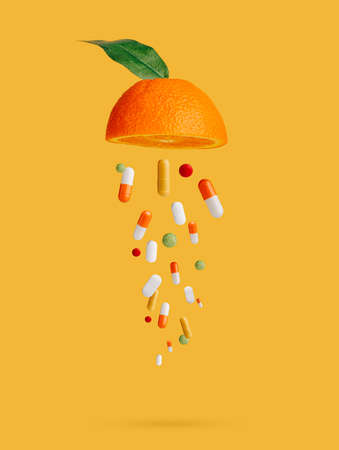 Vitamin medicine capsules raining from half sliced juicy orange against vibrant yellow background. Creative healthy organic food concept. Banner for juice bar.の写真素材