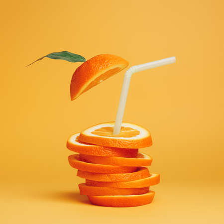Summer composition with fresh stacked orange slices and straw on vibrant orange background. Creative...