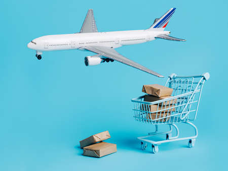 Plane flies around the shopping trolley and cardboard boxes on blue background. Creative cargo...