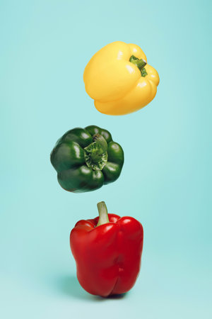 Variation of different color bell peppers flying in row against pastel green background. Creative organic vegetable concept. Banner for healthy food or diet with copy space.の写真素材