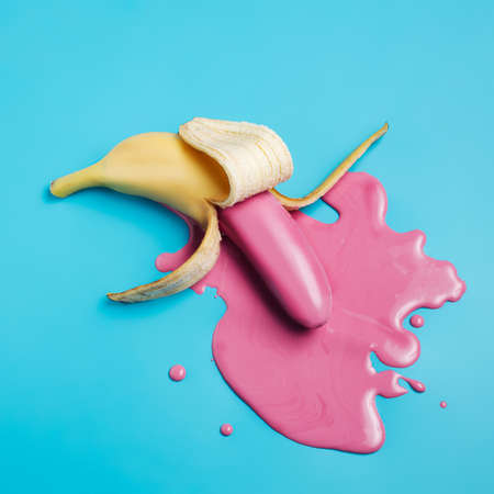 Peeled banana with pink fluid puddle against vibrant blue background. Minimal summer fruit concept. Vegetarian creative food banner with copy space. Flat lay, top view.の写真素材