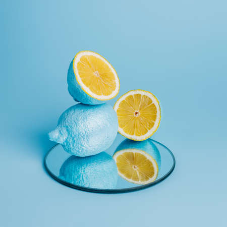 Blue painted lemons and half slices with mirror reflection on blue background. Creative summer fruit food concept. Empty mock up for cocktails, lemonade, smoothie or juice bar.の写真素材